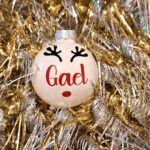 Boule de noël en verre blanc brillant avec prénom et décoration renne sur un fond doré