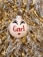 Boule de noël en verre blanc brillant avec prénom et décoration renne sur un fond doré
