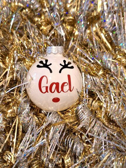 Boule de noël en verre blanc brillant avec prénom et décoration renne sur un fond doré