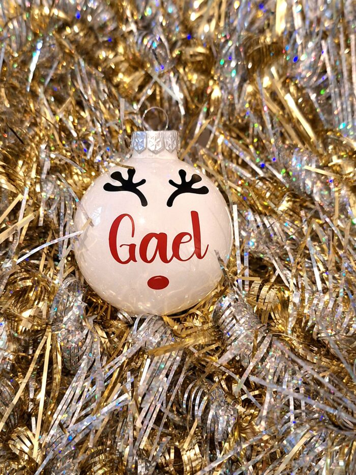 Boule de noël en verre blanc brillant avec prénom et décoration renne sur un fond doré