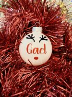 Boule de noël en verre blanc brillant avec prénom et décoration renne sur un fond rouge