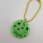 Pendentif en résine, fond vert avec petits avions et le prénom Héctor. Chaîne à billes jaune